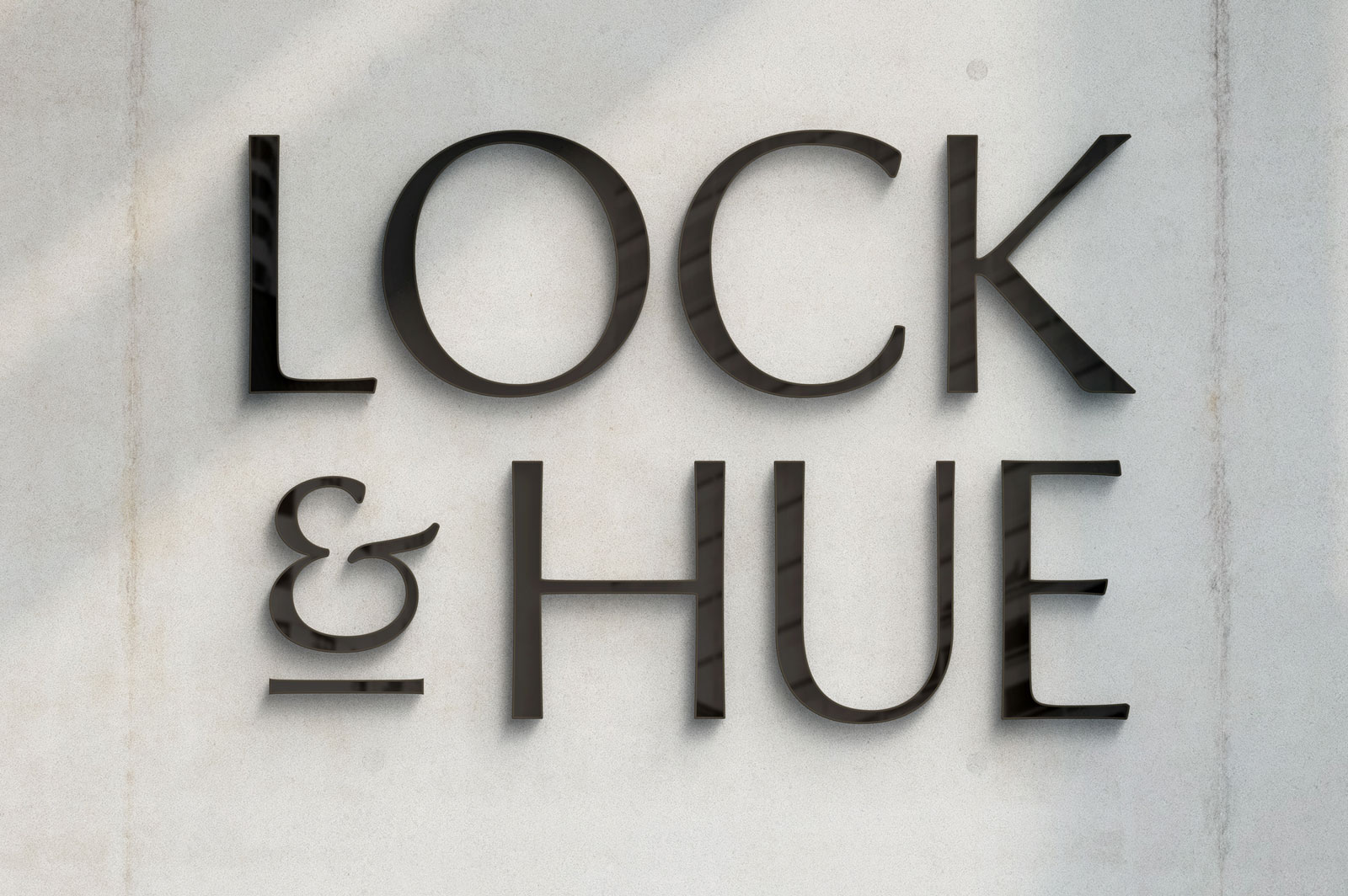 The Lock & Hue logo made from darkly stained wood placed on a white wall