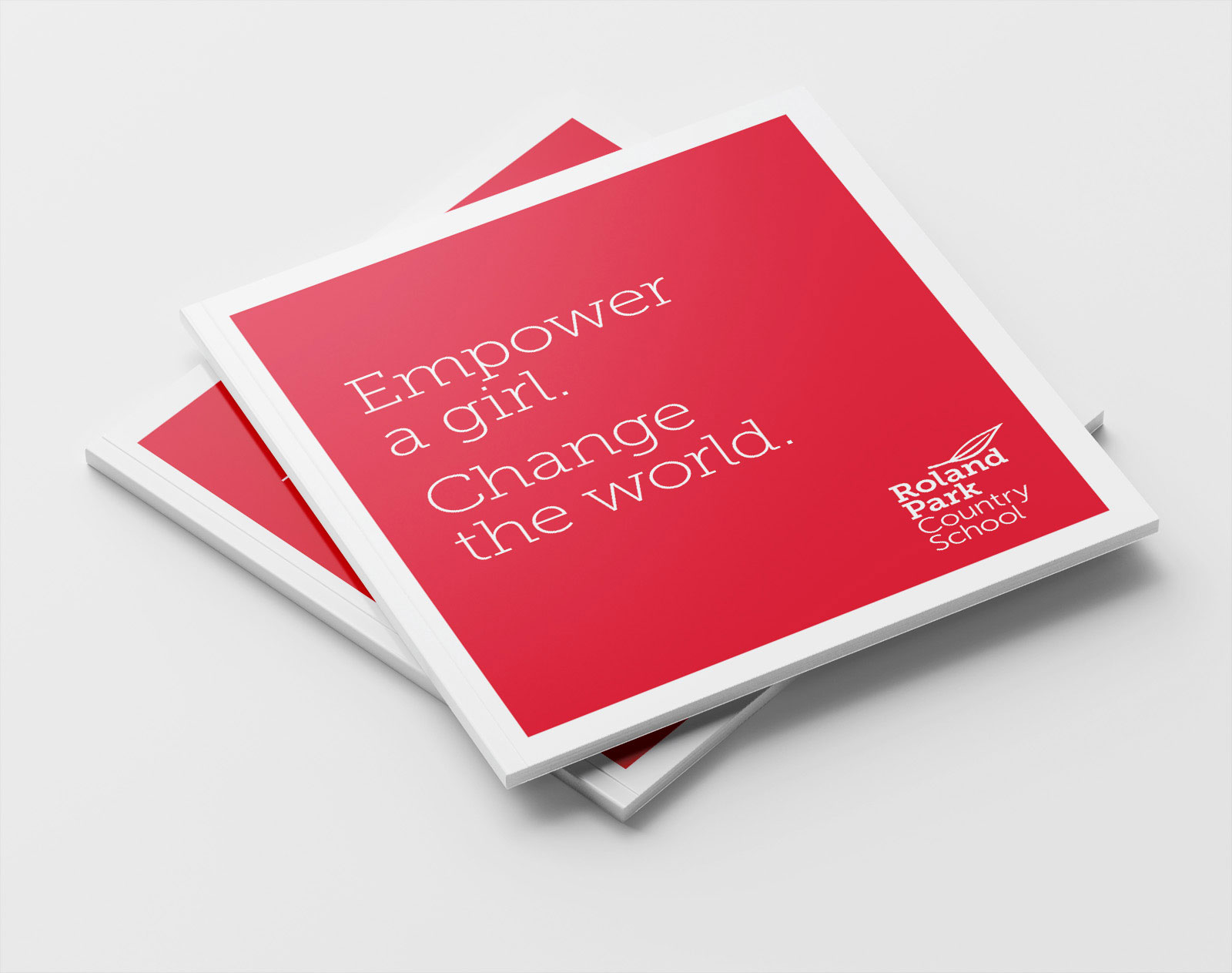 A stack of Roland Park Country Schook report books featuring white text that reads 'Empower a girl. Change the world' on a red background